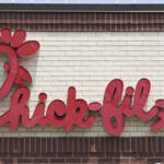 Chick-fil-A logo sign in red cursive on a beige brick wall.