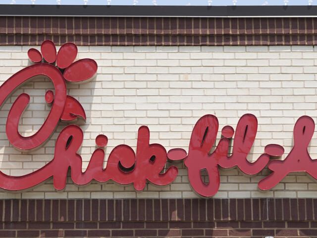 Chick-fil-A logo sign in red cursive on a beige brick wall.