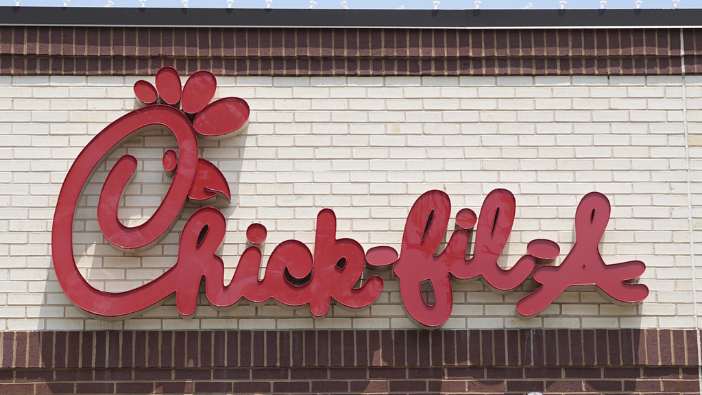Chick-fil-A logo sign in red cursive on a beige brick wall.