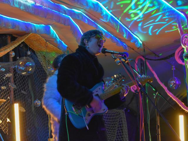 Lead singer and guitarist of a psych-rock band sings into a microphone on an underwater-themed stage.