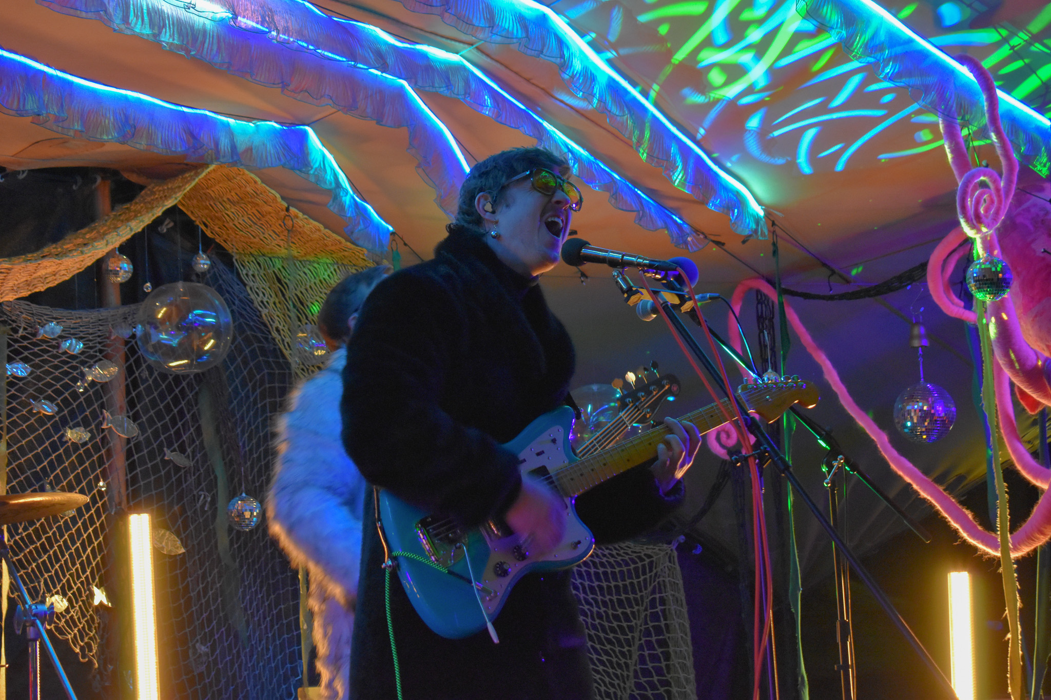 Lead singer and guitarist of a psych-rock band sings into a microphone on an underwater-themed stage.