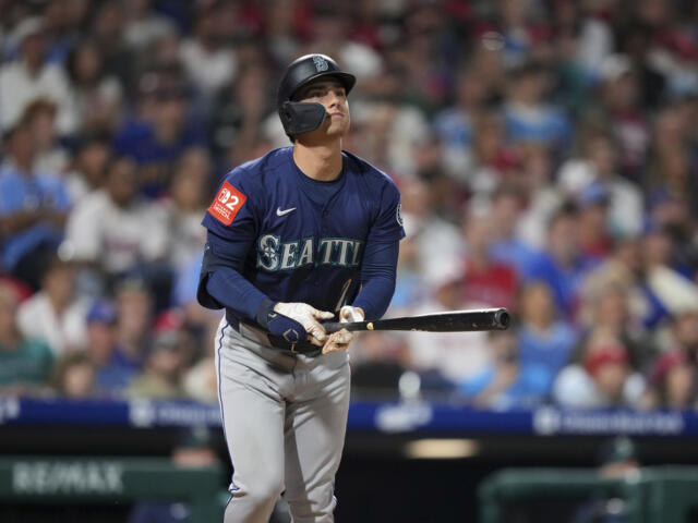Seattle Mariners batter in navy jersey stands at the plate, gripping a bat with a face-guard helmet.