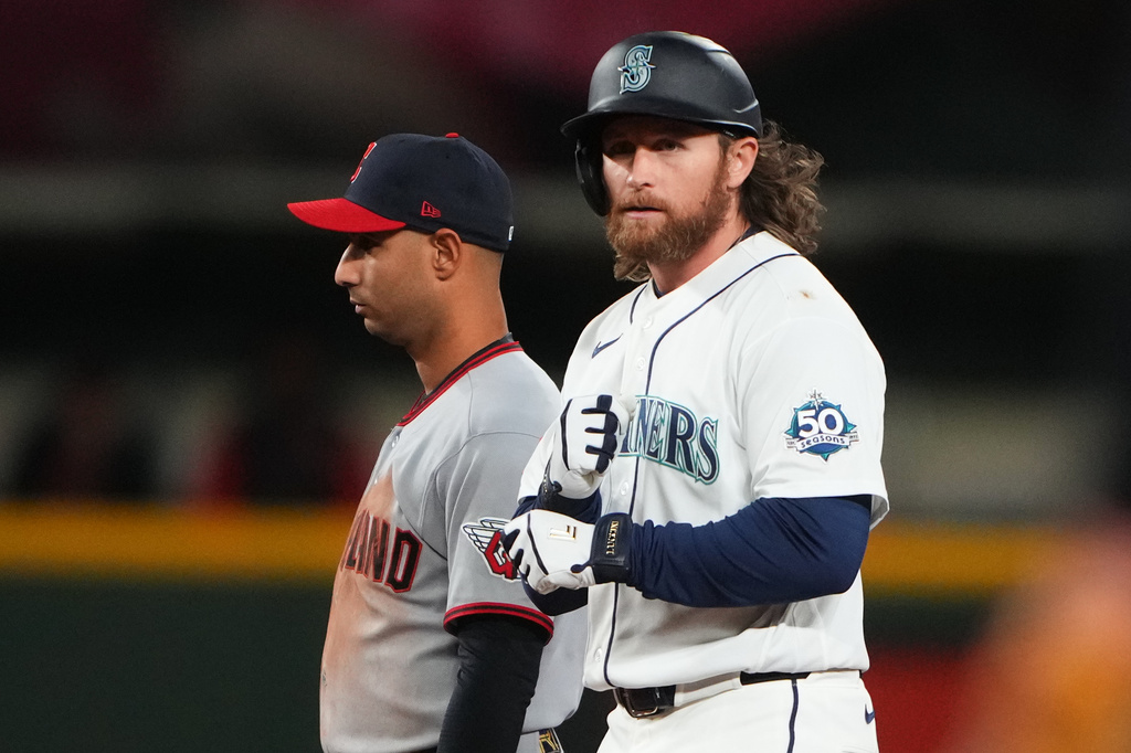 Seattle Mariners batter in white uniform with helmet and 50 Seasons patch stands at the plate, while a Cleveland pitcher/infielder in gray with a red cap lingers behind him.