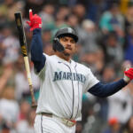 Seattle Mariners batter celebrates a hit, raising one arm with bat in the air on the field.