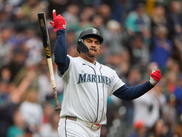 Seattle Mariners batter celebrates a hit, raising one arm with bat in the air on the field.