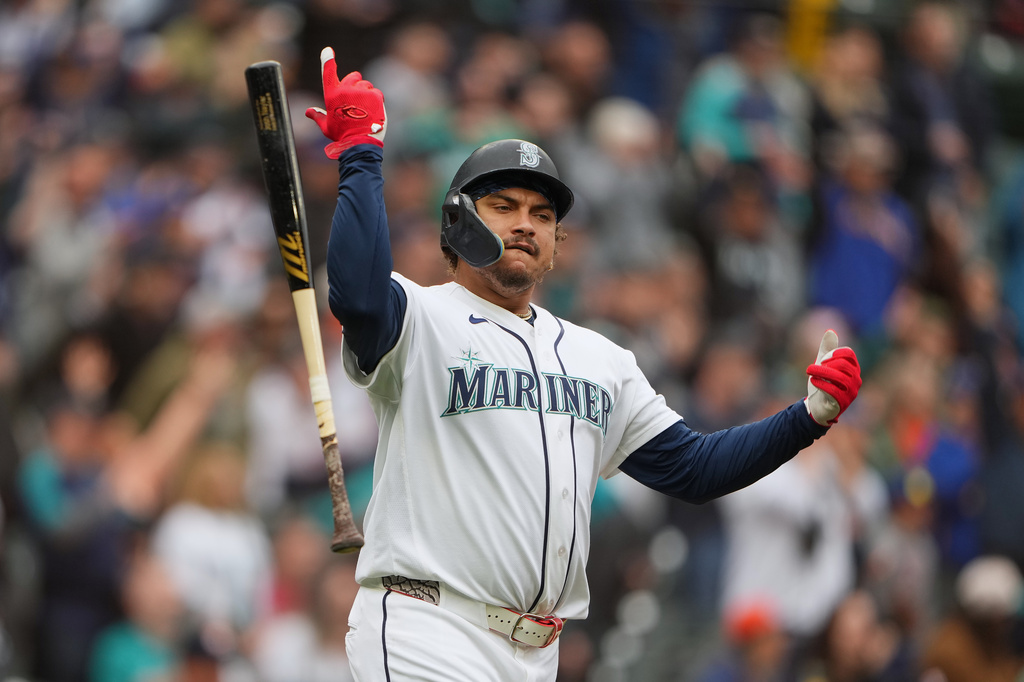 Seattle Mariners batter celebrates a hit, raising one arm with bat in the air on the field.