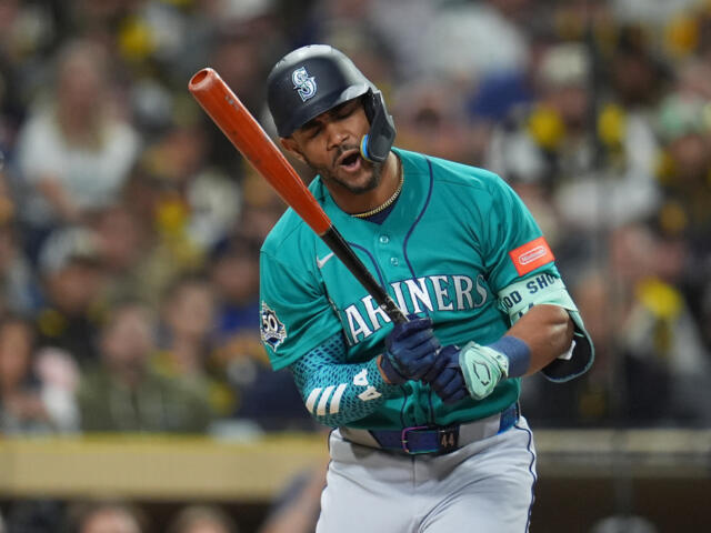 Mariners batter mid-swing in teal uniform with orange bat during a baseball game, crowd in background