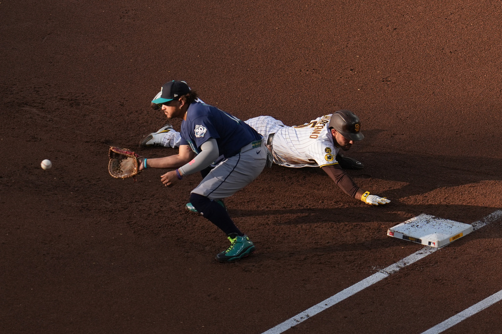 Baseball infield action: fielder in blue reaches for a ground ball as a baserunner slides toward the base beside him.