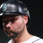 Baseball player wearing a dark helmet with the Seattle Mariners logo, looking down with a beard.