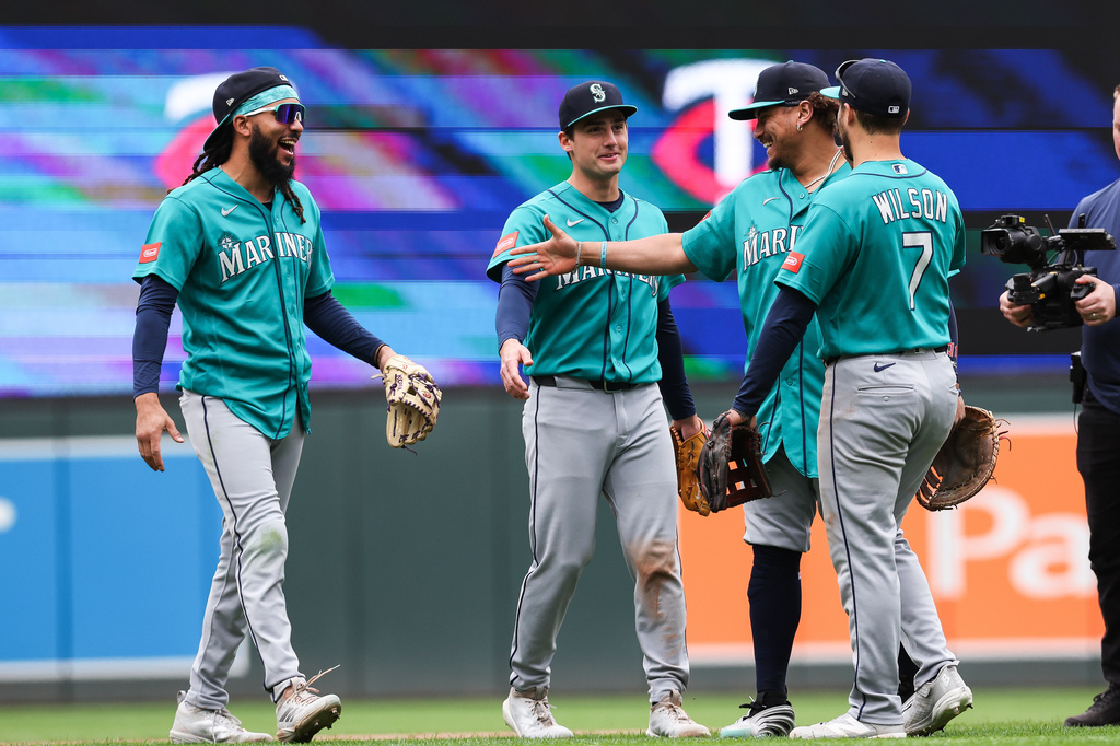 Seattle Mariners players in teal uniforms celebrate on the field, high-fiving and smiling together.