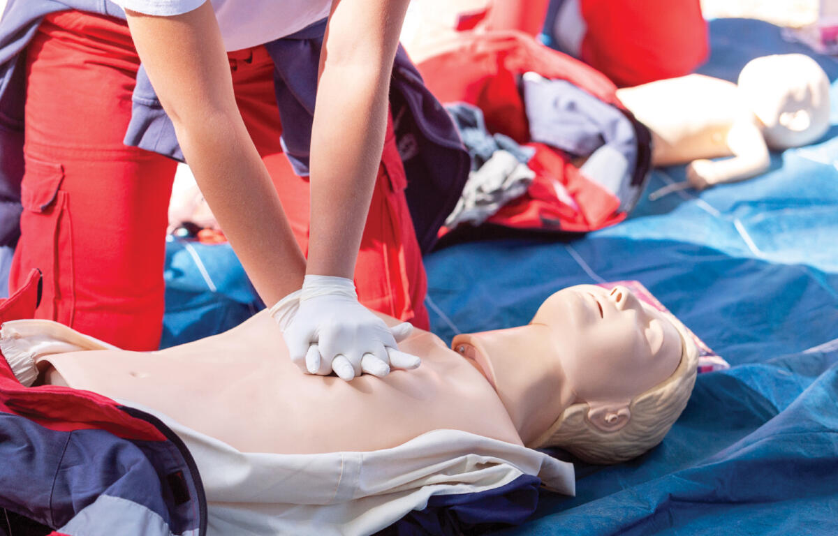 Person in red pants practicing chest compressions on a CPR manikin during a training drill with gloved hands.