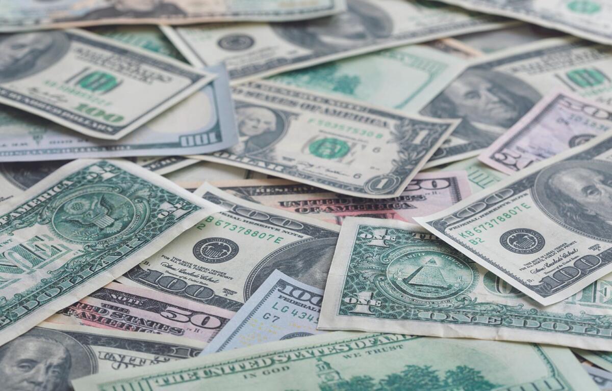 Pile of assorted U.S. dollar bills scattered and overlapping on a flat surface (including $1, $5, $10, and $100 notes).