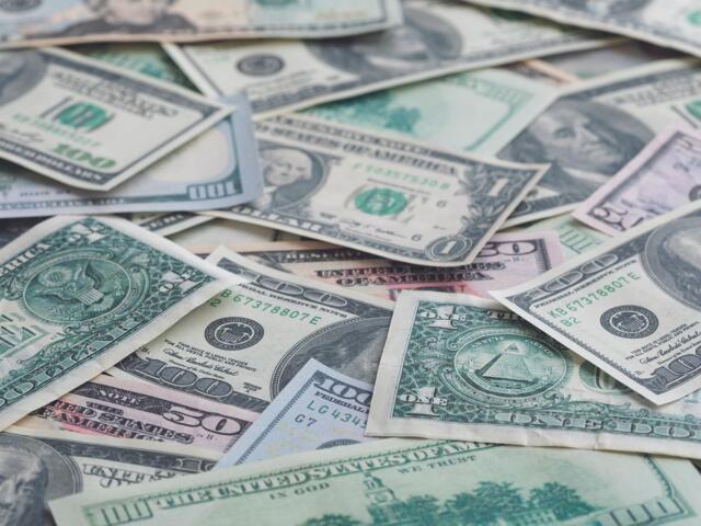 Pile of assorted U.S. dollar bills scattered and overlapping on a flat surface (including $1, $5, $10, and $100 notes).