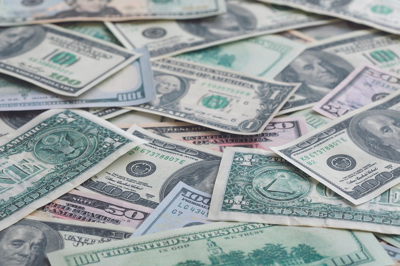 Pile of assorted U.S. dollar bills scattered and overlapping on a flat surface (including $1, $5, $10, and $100 notes).