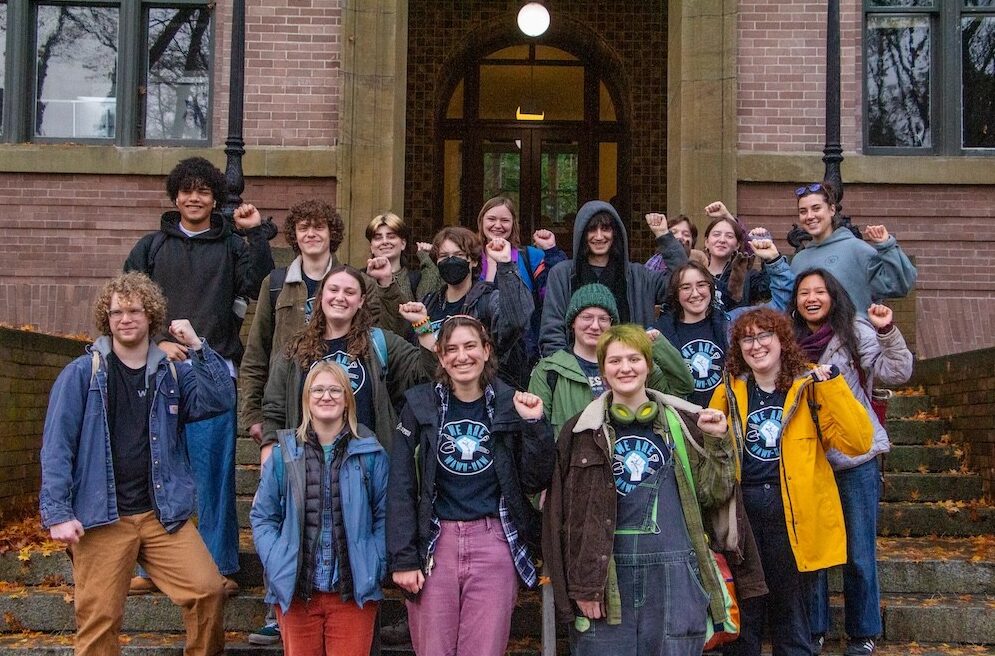 Group of diverse students posing on campus steps, fists raised in solidarity.