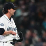 Mariners pitcher in white uniform holding glove, facing left, on the mound during a game in a crowded stadium