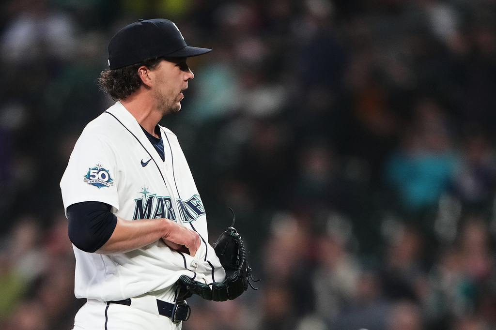 Mariners pitcher in white uniform holding glove, facing left, on the mound during a game in a crowded stadium