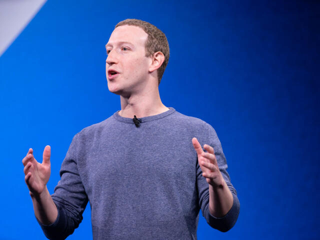 Man in a blue sweater giving a presentation on stage, gesturing with his hands.