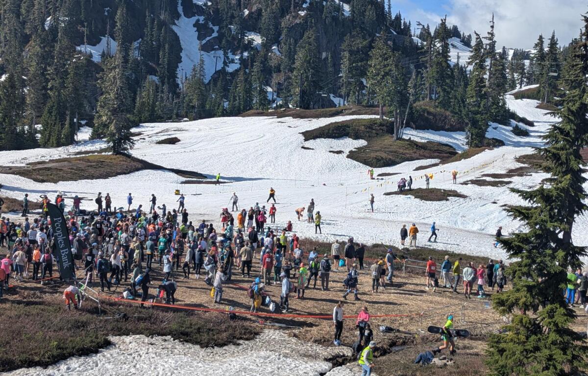 Large crowd of skiers and spectators on a snow-covered slope, with evergreen trees and a chairlift in the background.