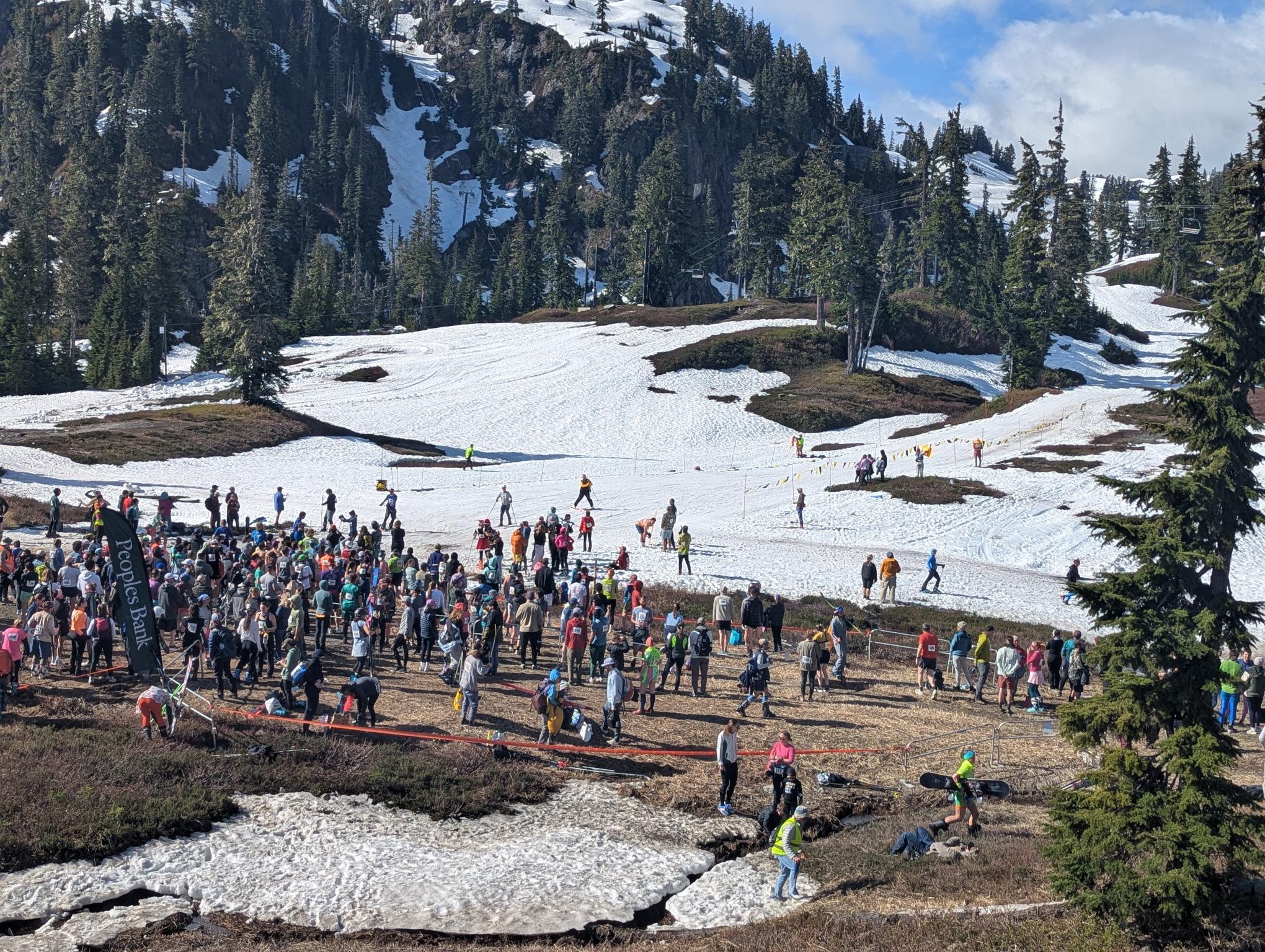 Large crowd of skiers and spectators on a snow-covered slope, with evergreen trees and a chairlift in the background.