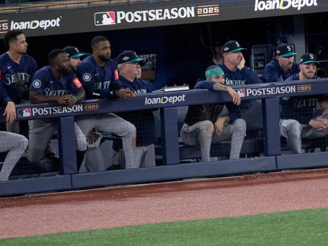 Seattle Mariners players in the dugout during a postseason game, leaning on the railing and watching the field, with Postseason 2025 and loanDepot signage visible.