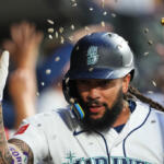 Baseball player in Seattle Mariners uniform raises his gloved hand in celebration with confetti falling around him.