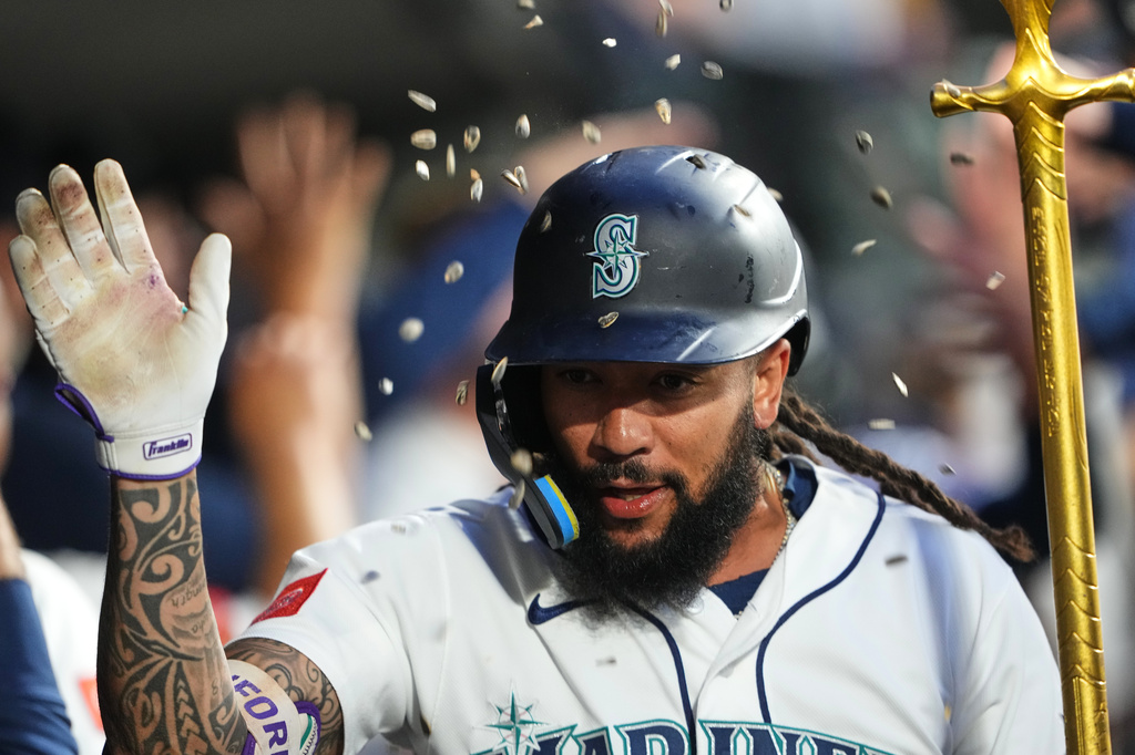 Baseball player in Seattle Mariners uniform raises his gloved hand in celebration with confetti falling around him.