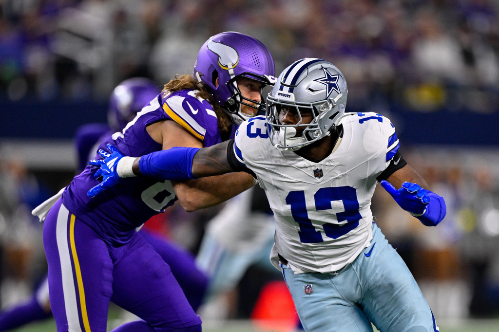 Dallas Cowboys player in white (#13) being tackled by a Minnesota Vikings defender in purple during an NFL game on the field.