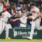 Two Braves players exchange a high-five on the baseball field as a crowd cheers in the background.