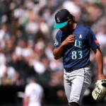 Baseball pitcher in Mariners uniform walking on the mound, glove in hand, focused on the game.