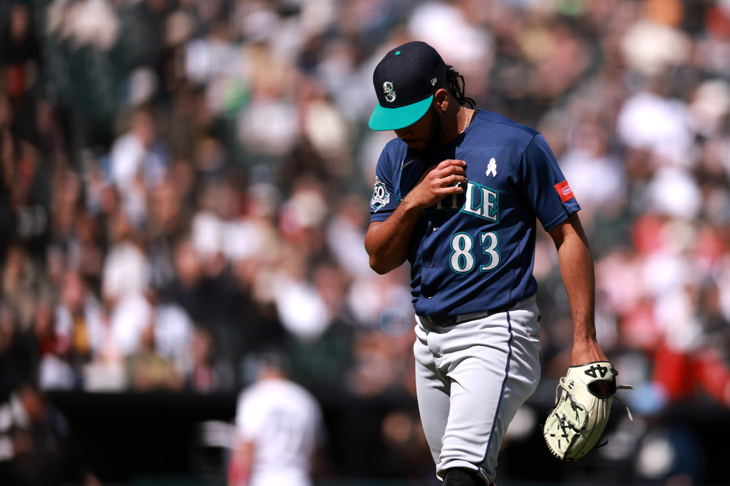 Baseball pitcher in Mariners uniform walking on the mound, glove in hand, focused on the game.