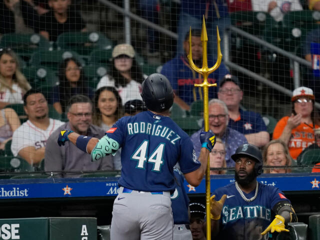 Baseball player Rodríguez #44 in blue uniform stands at the dugout, holding a tall gold trident while a teammate looks on.