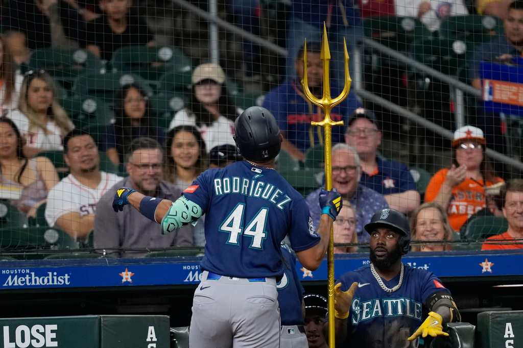 Baseball player Rodríguez #44 in blue uniform stands at the dugout, holding a tall gold trident while a teammate looks on.