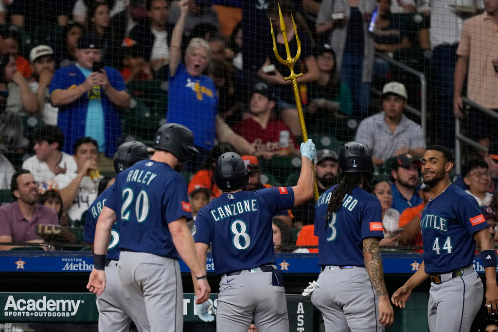 Baseball players in blue jerseys celebrate in the dugout as one raises a gold trident overhead while fans cheer behind them in the stands.