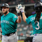 Two Seattle Mariners players in teal uniforms high-five on the field during a game.