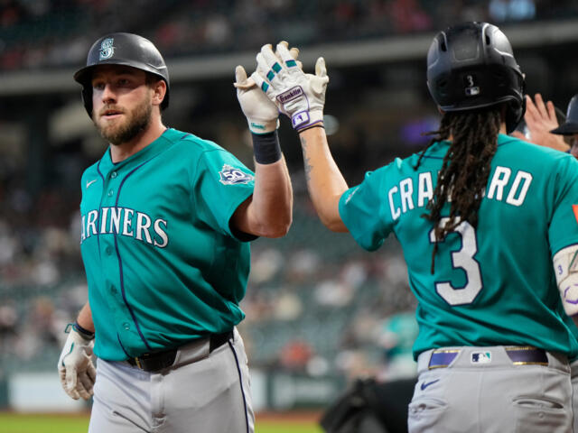 Two Seattle Mariners players in teal uniforms high-five on the field during a game.