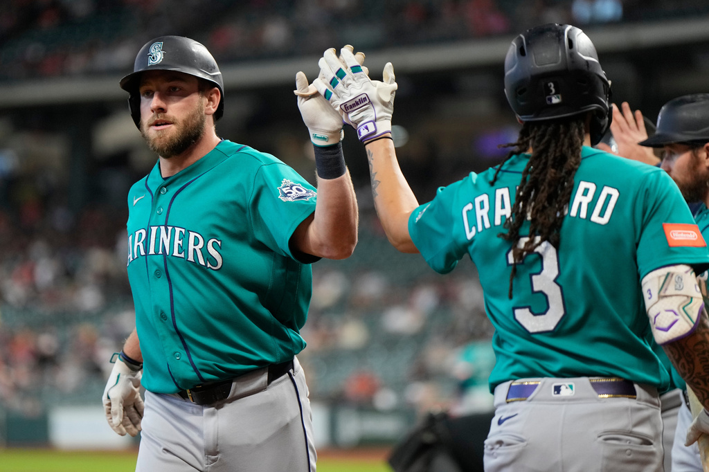 Two Seattle Mariners players in teal uniforms high-five on the field during a game.