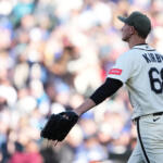 Baseball pitcher with jersey reading 'KIRBY' and number 68 adjusts his glove during a game, crowd in the stands blurred behind him.