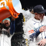 Two Seattle Mariners players celebrate, pouring an orange Gatorade jug over one player's head as water sprays around them in white uniforms.