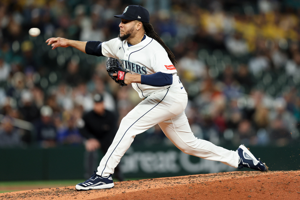 Seattle Mariners pitcher in white uniform mid-pitch on the mound during a game with a blurred crowd in the background.