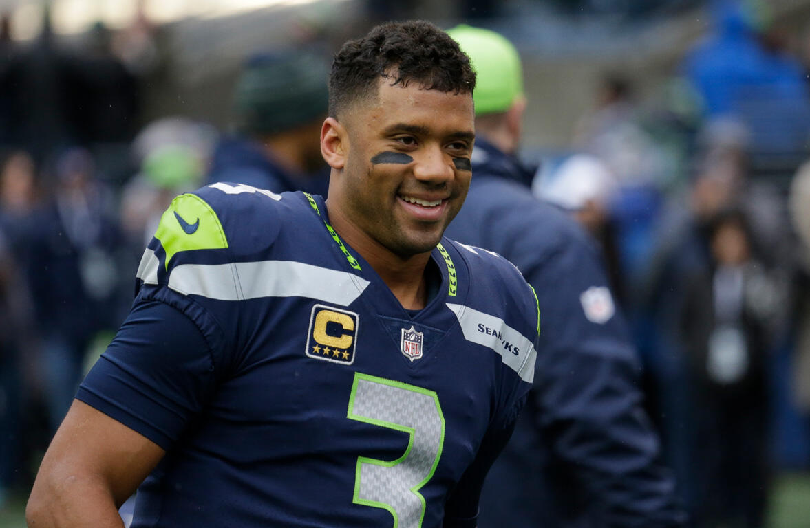 Seahawks player wearing #3 jersey with captain patch, smiling on the field in navy and neon-green uniform.