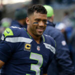 Seahawks player wearing #3 jersey with captain patch, smiling on the field in navy and neon-green uniform.
