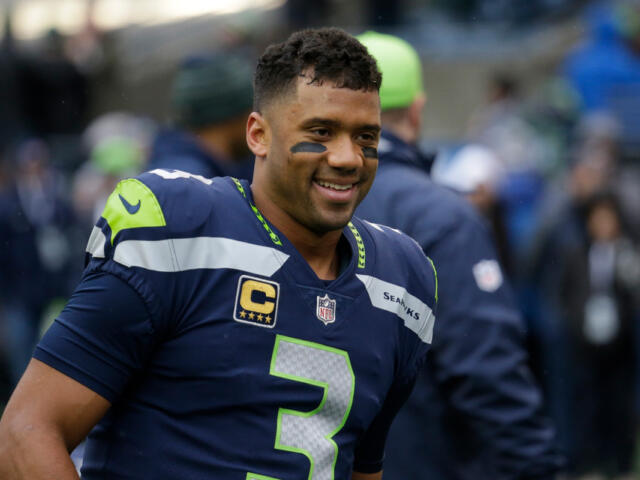 Seahawks player wearing #3 jersey with captain patch, smiling on the field in navy and neon-green uniform.