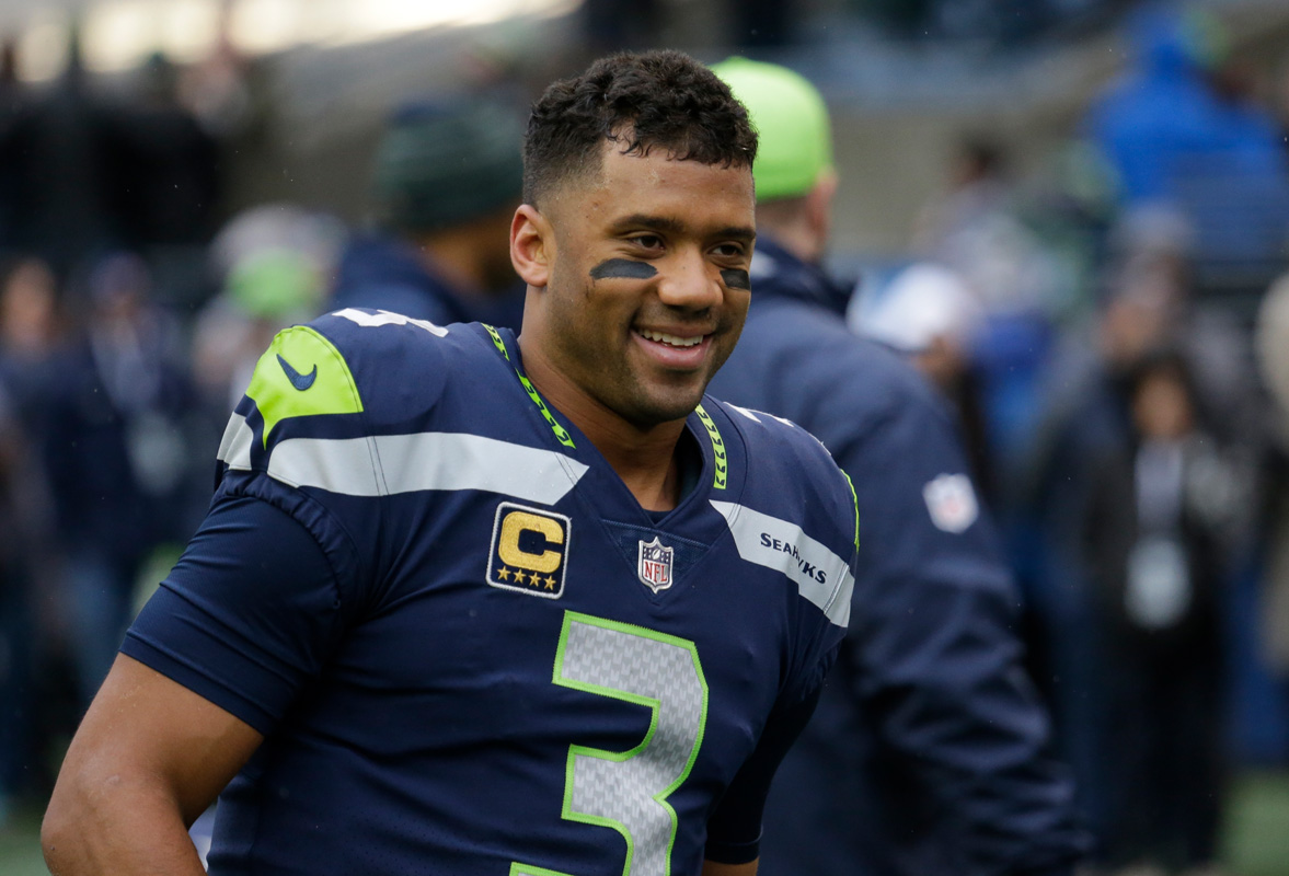 Seahawks player wearing #3 jersey with captain patch, smiling on the field in navy and neon-green uniform.
