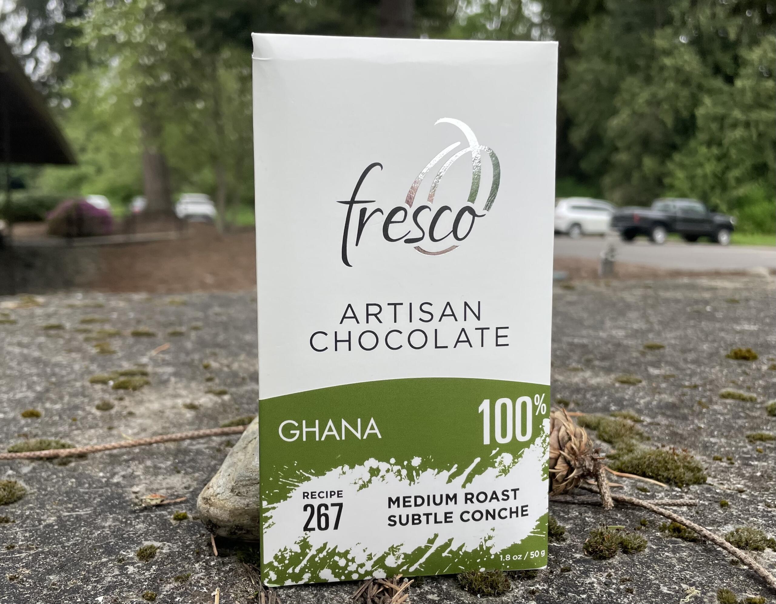 Close-up of a Fresco artisan chocolate box showing Ghana 100% with green accent at the bottom outside on the ground.