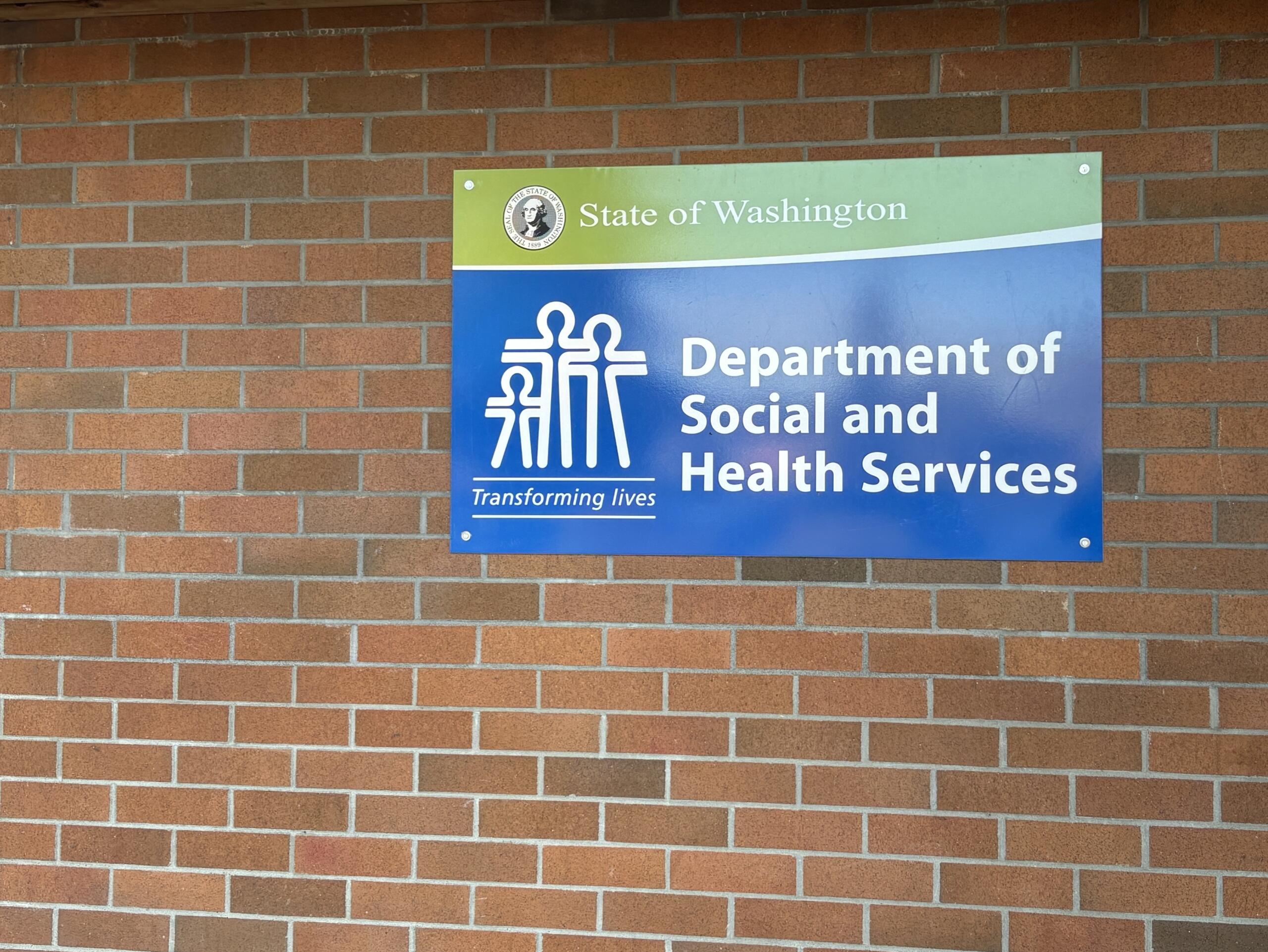 Blue and green Department of Social and Health Services sign mounted on a brick wall in Washington state.
