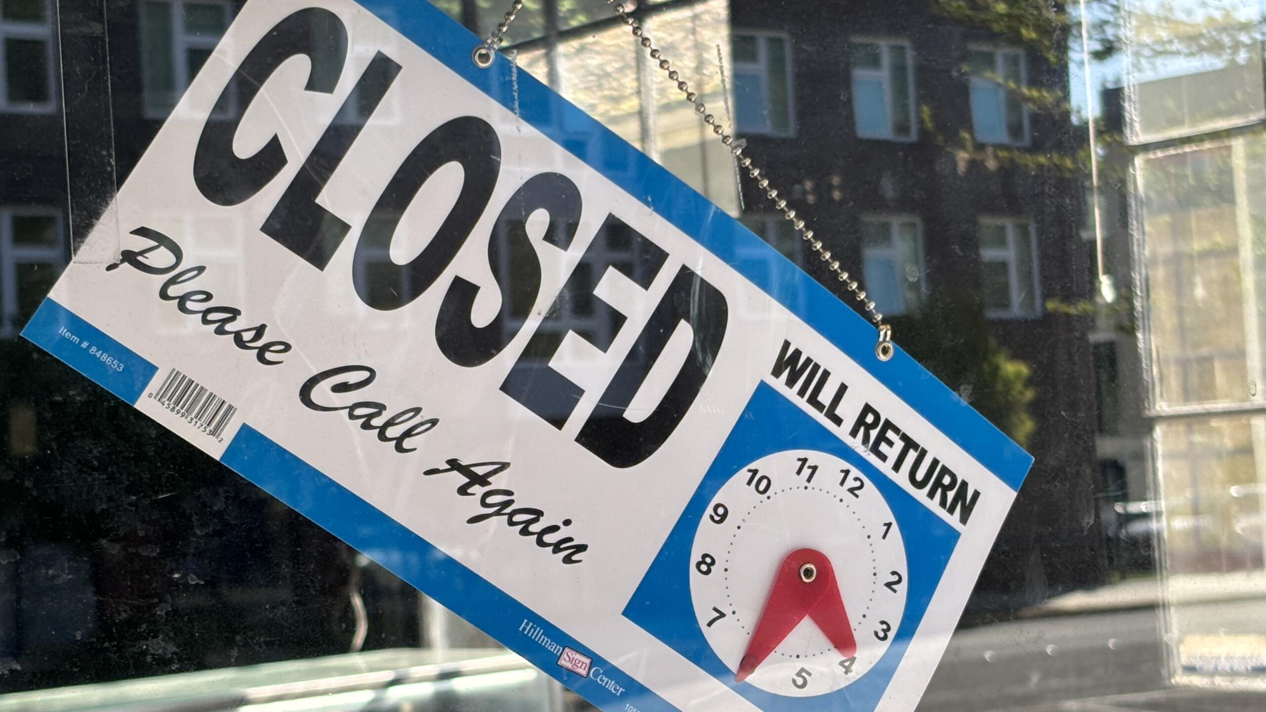 Storefront window displaying a large 'CLOSED' notice with 'Will return' text and a clock illustration showing return hours.