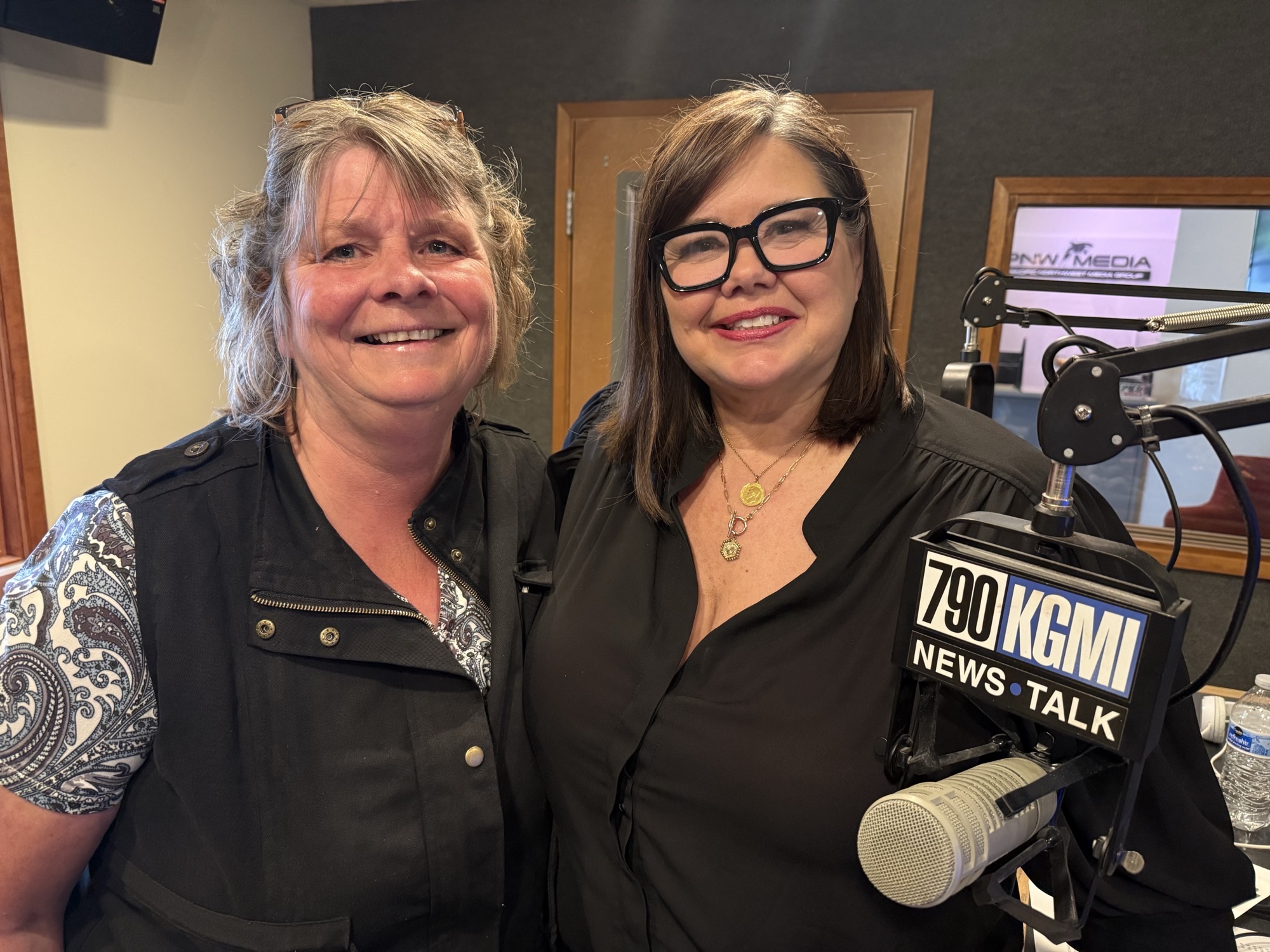 Two women posing for a selfie in a radio studio, smiling, with microphones and a 790 KGM News Talk sign visible in the foreground behind them.