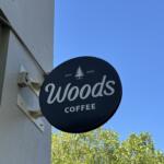 Dark blue circular Woods Coffee sign with white script and a small tree logo, mounted on a light building under a clear blue sky