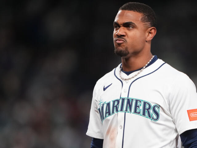 Baseball player in Mariners uniform making a pouty, determined expression on the field.